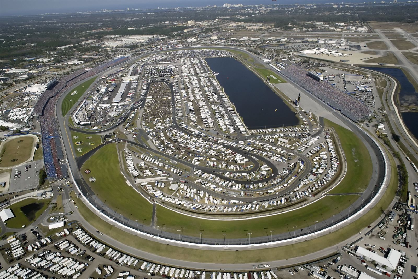 Aerial view of a race track oval filled with campers and motor homes around a lake in the infield