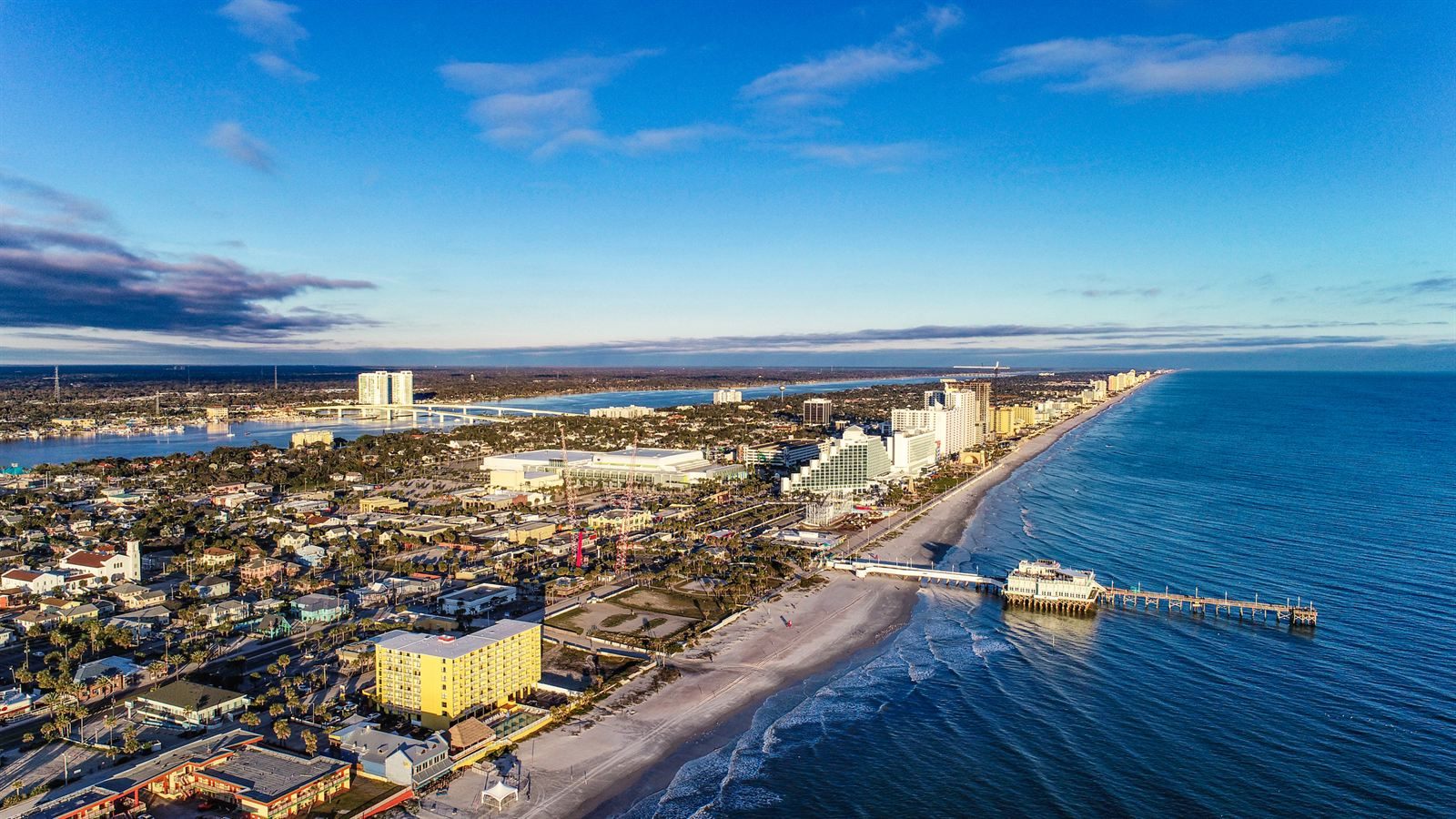 Aerial view of Daytona Beach, with the pier reaching into the ocean, beachfront hotels and the Halifax River behind the town